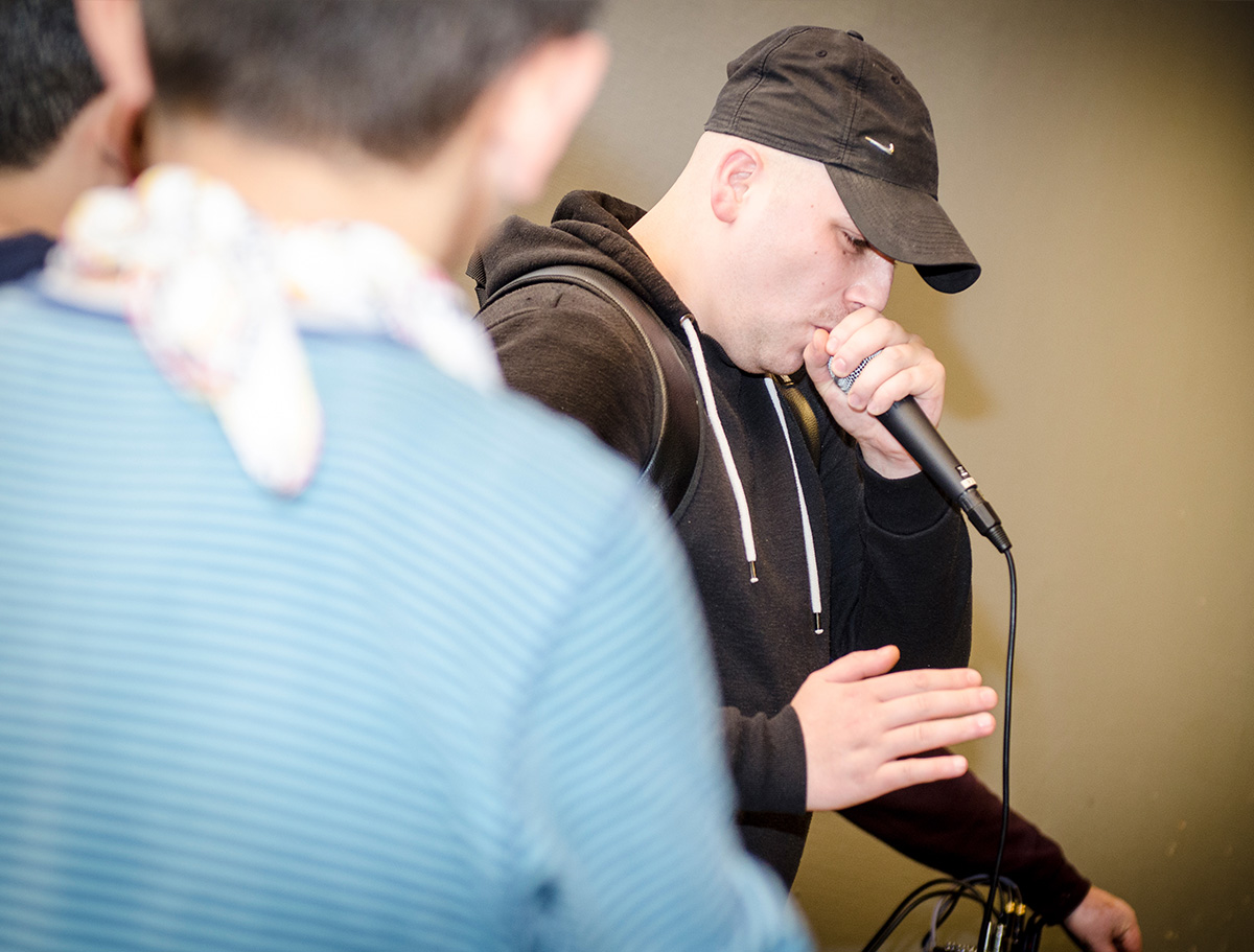 Ein junger Mann rapt in dein Mikro und zwei Jungen hören zu