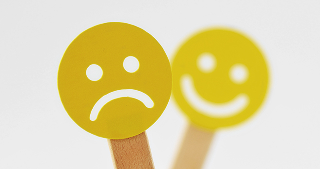 Ein trauriger Smiley, im Hintergrund ein lächelnder Smiley